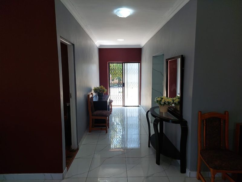 A well-lit hallway featuring polished tiled flooring, neutral grey and accent red walls, and a secure sliding door entrance.