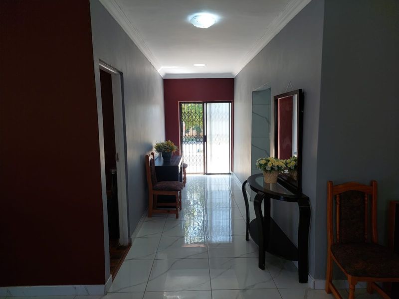 A well-lit hallway featuring polished marble-look floor tiles, grey and deep red wall finishes, and a secure sliding door leading to the exterior.
