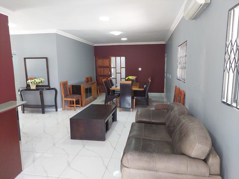 Spacious open-plan living and dining area featuring polished marble-look floor tiles, neutral grey walls with a feature wall, and integrated air conditioning.