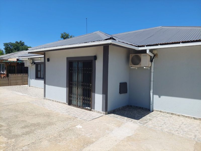 Rear exterior view of the commercial property featuring a paved patio, sliding glass door with security gate, and wall-mounted air conditioning unit.