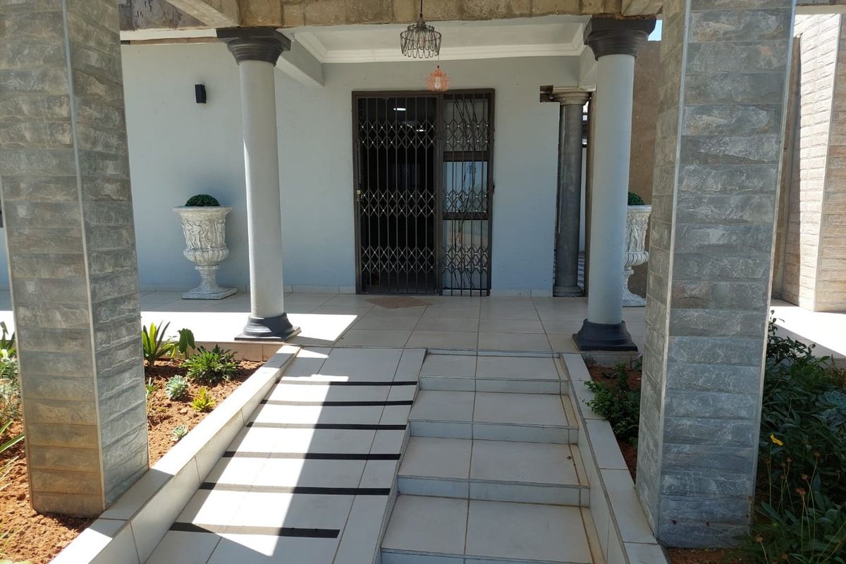 Covered entrance featuring a tiled porch, wheelchair ramp, and stone-clad support columns with a secure metal gate.
