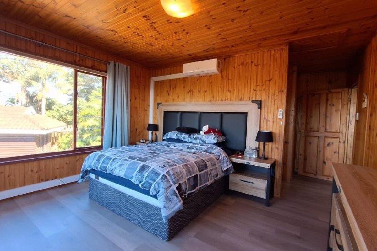 A bedroom featuring extensive timber wall and ceiling paneling, a large window providing natural light, and a wall-mounted split-system air conditioning unit.