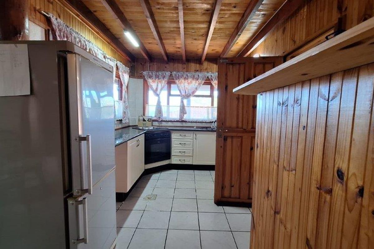 A functional kitchen featuring timber-paneled walls and ceilings, tiled flooring, built-in cabinetry, and integrated cooking appliances.