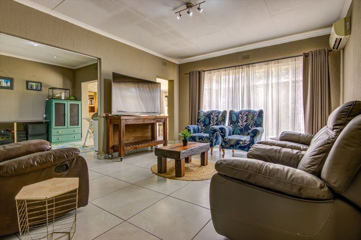 Spacious living room featuring neutral tiled flooring, track lighting, and a wall-mounted air conditioning unit, offering a comfortable and functional living space.