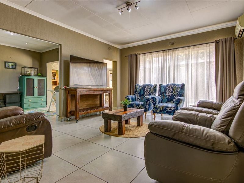 Spacious living room featuring neutral tiled flooring, track lighting, and a wall-mounted air conditioning unit, offering a comfortable and functional living space.