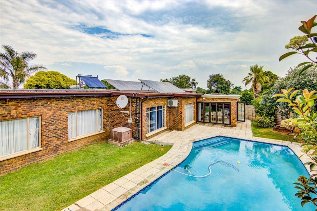 Rear view of the property featuring a swimming pool, paved patio area, brick exterior, and roof-mounted solar panels and water heating system.