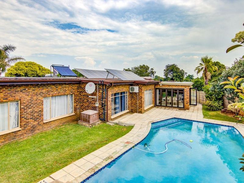 Rear view of the property featuring a swimming pool, paved patio area, brick exterior, and roof-mounted solar panels and water heating system.