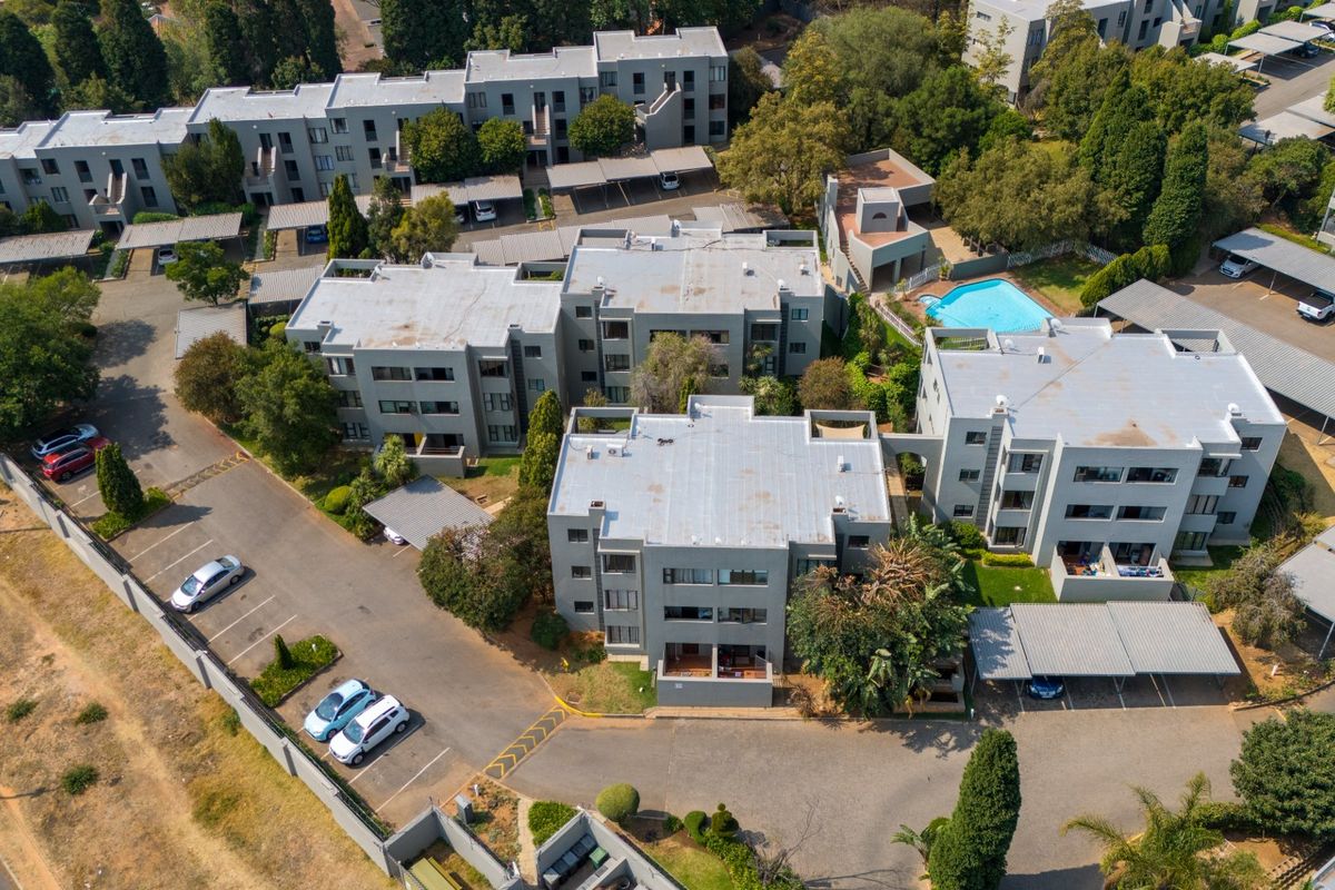 Aerial view of an apartment complex featuring multiple residential blocks, a swimming pool, covered parking bays, and landscaped grounds.