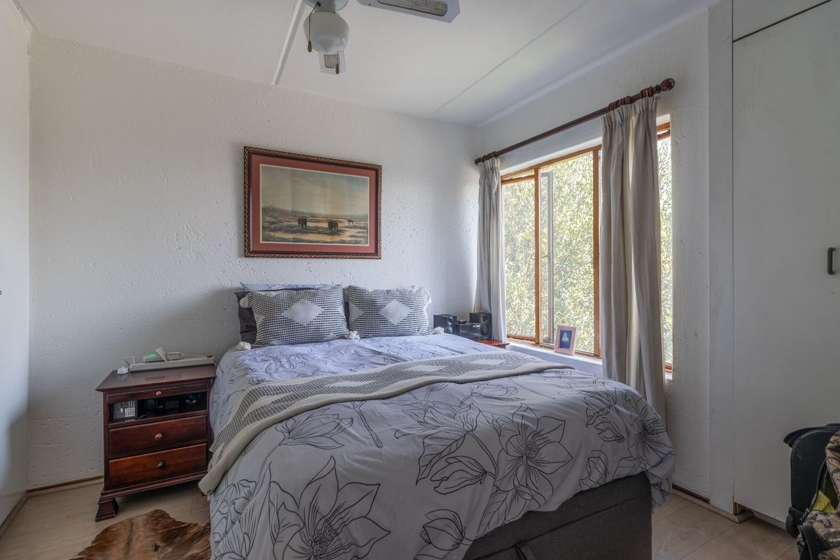 A cozy bedroom featuring laminate flooring, a built-in wardrobe, and a ceiling fan, with natural light provided by a large window.