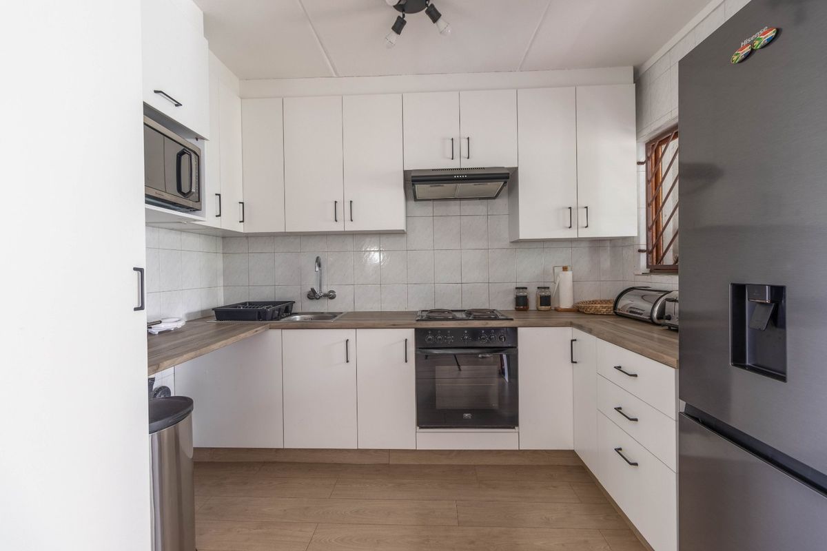 A well-maintained kitchen featuring white cabinetry, wood-look laminate countertops, a built-in oven with gas hob, and a tiled backsplash.