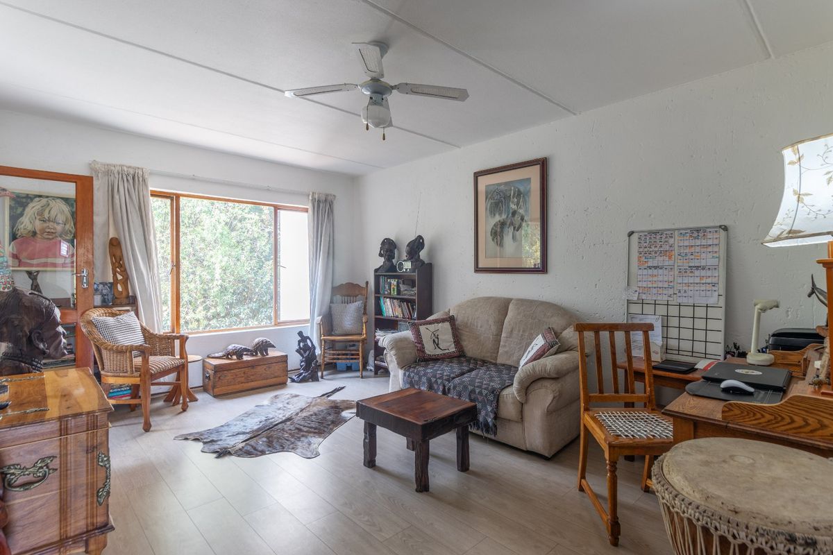 A bright living room featuring laminate flooring, a ceiling fan, and a large window providing natural light.