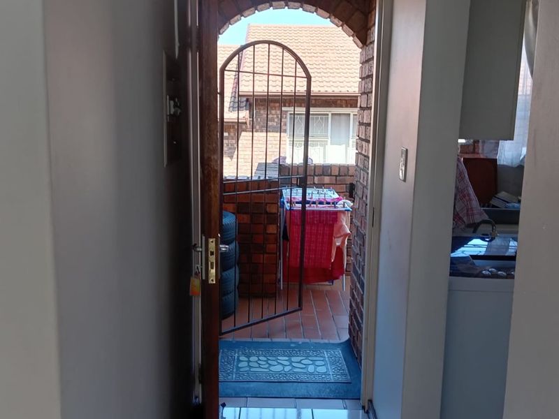 A view through an open doorway onto a small balcony featuring a brick archway, security gate, and tiled flooring.