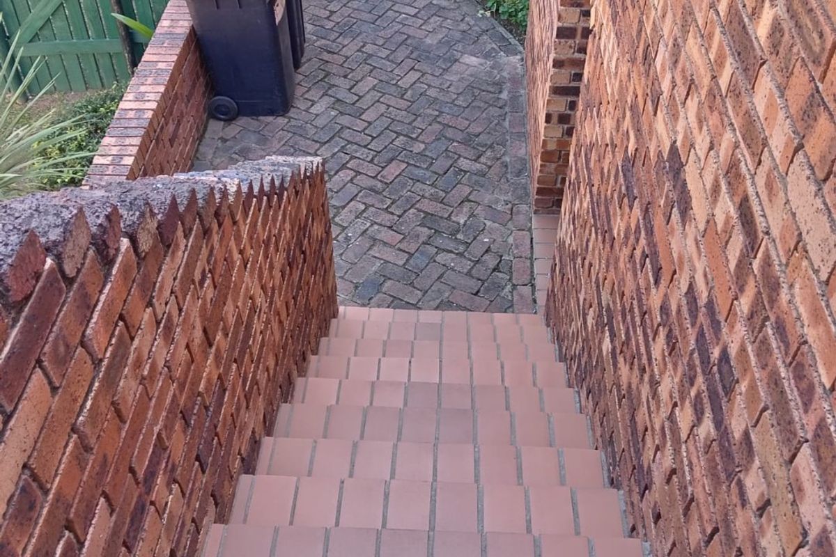 An outdoor brick staircase leading down to a paved pathway and garden area, featuring sturdy brick retaining walls.