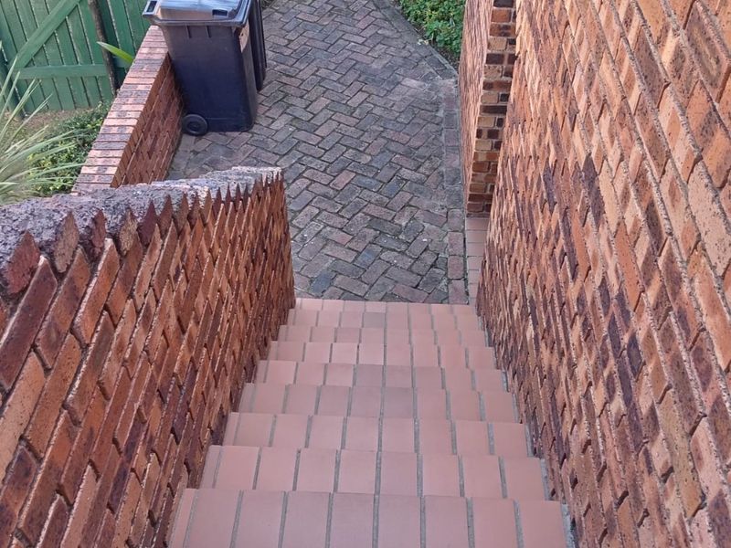 An outdoor brick staircase leading down to a paved pathway and garden area, featuring sturdy brick retaining walls.