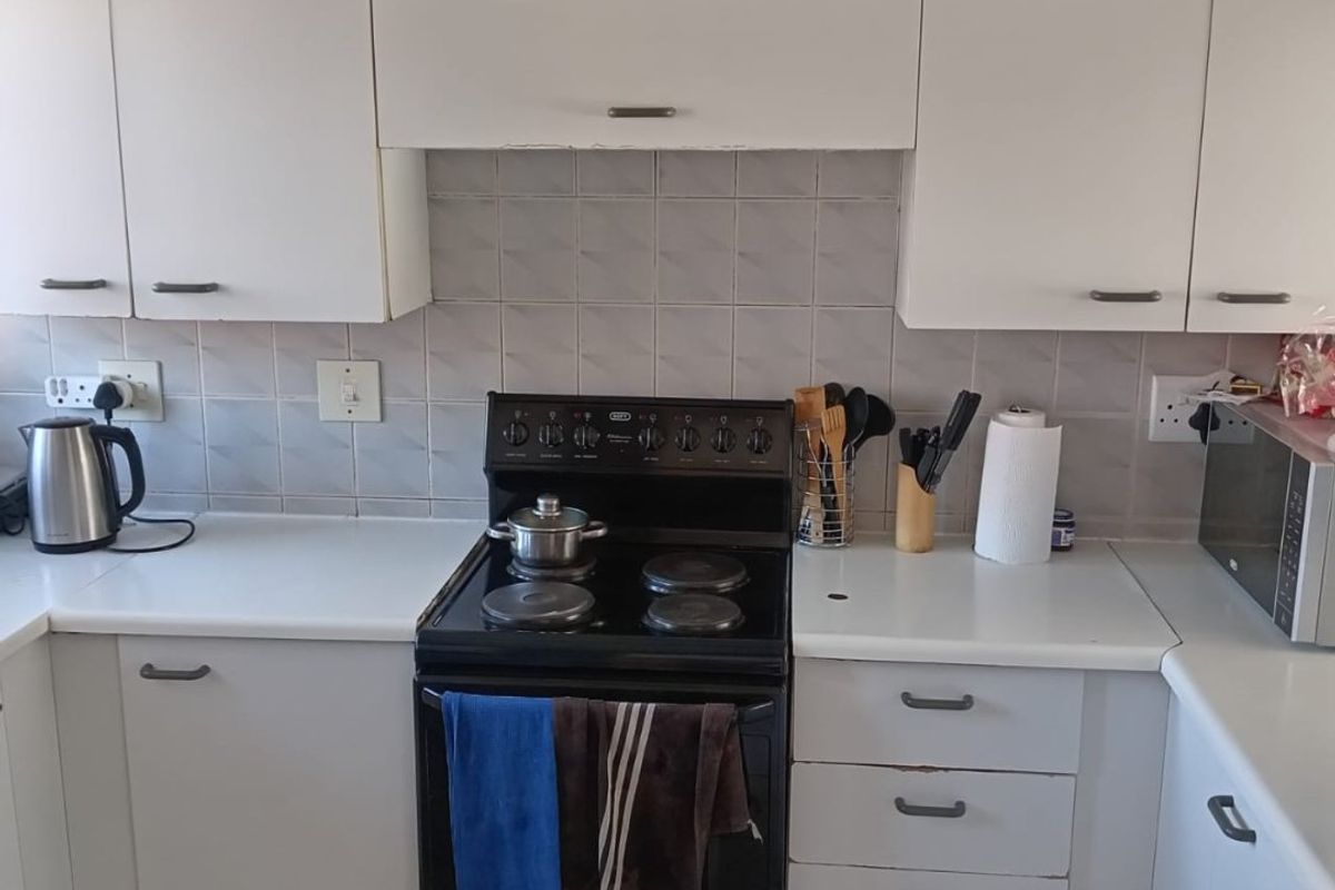 A functional kitchen featuring white cabinetry, laminate countertops, a ceramic tile backsplash, and a built-in electric stove and oven unit.