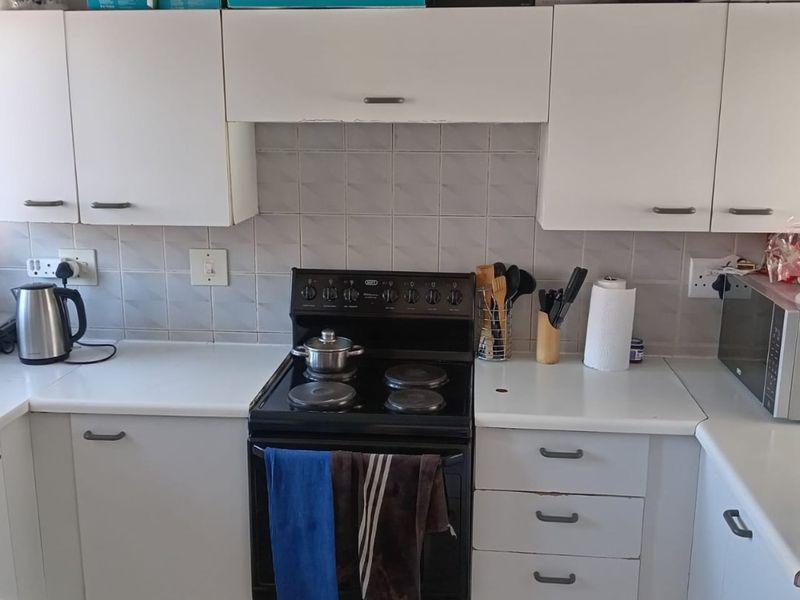 A functional kitchen featuring white cabinetry, laminate countertops, a ceramic tile backsplash, and a built-in electric stove and oven unit.
