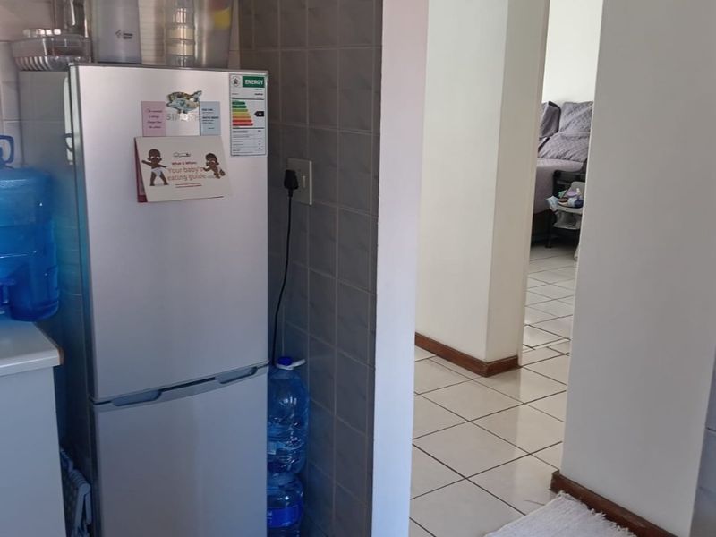 A functional kitchen area featuring ceramic wall and floor tiling, providing a clean and practical space with direct access to the hallway.