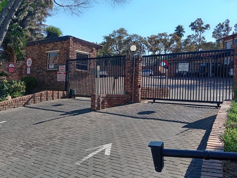Secure gated entrance to the apartment complex featuring a brick guardhouse and paved driveway access.