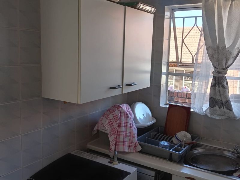 A compact laundry area featuring wall-mounted cabinetry, a stainless steel sink, and tiled wall finishes with a window providing natural light.