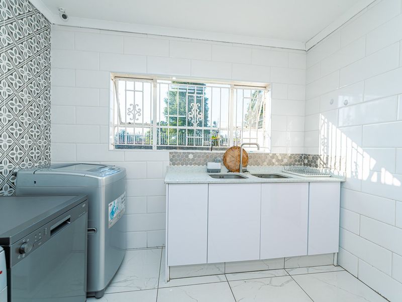 A clean and functional laundry room featuring white cabinetry, a double basin sink, tiled splashbacks, and tiled flooring.