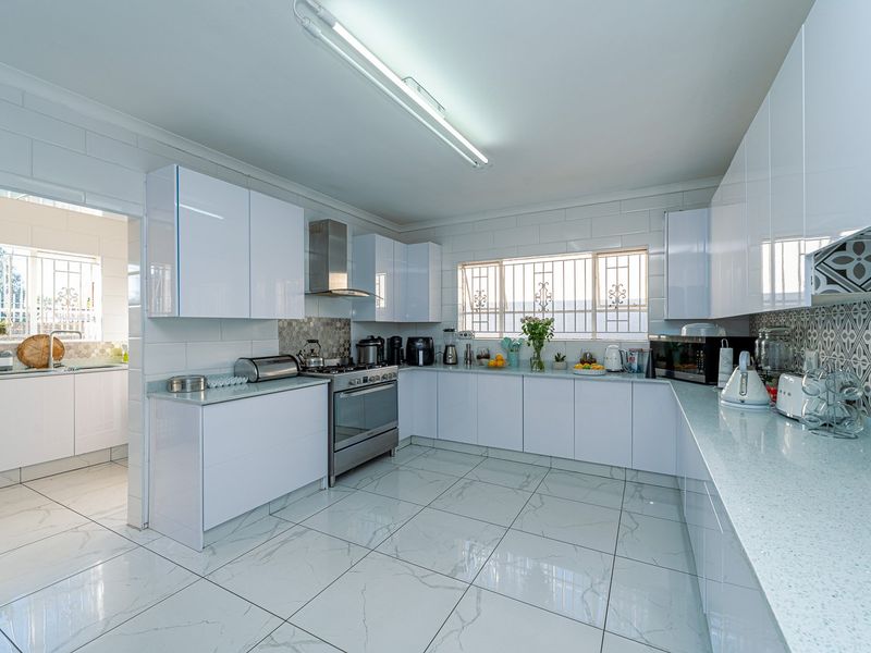 Modern kitchen featuring white high-gloss cabinetry, stone countertops, stainless steel appliances, and polished marble-look floor tiles with an adjoining scullery area.