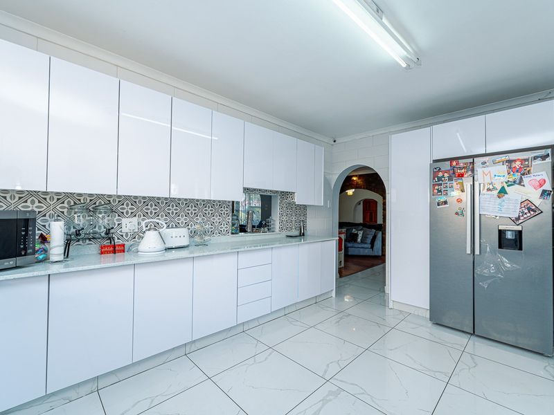 Modern kitchen featuring white gloss cabinetry, stone countertops, patterned tile backsplash, and large format porcelain floor tiles with an arched entryway.