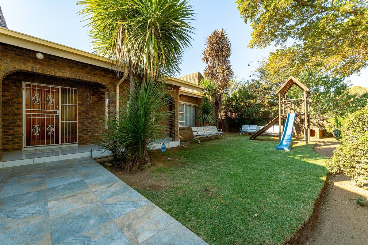 A rear exterior view featuring a brick facade, a tiled patio area, and a well-maintained garden with mature trees.