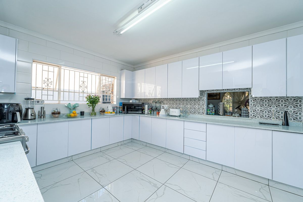 Modern kitchen featuring white gloss cabinetry, stone countertops, patterned tile backsplash, and large format marble-look floor tiles with ample storage space.