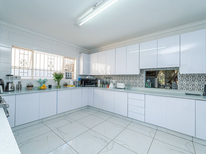 Modern kitchen featuring white gloss cabinetry, stone countertops, patterned tile backsplash, and large format marble-look floor tiles with ample storage space.