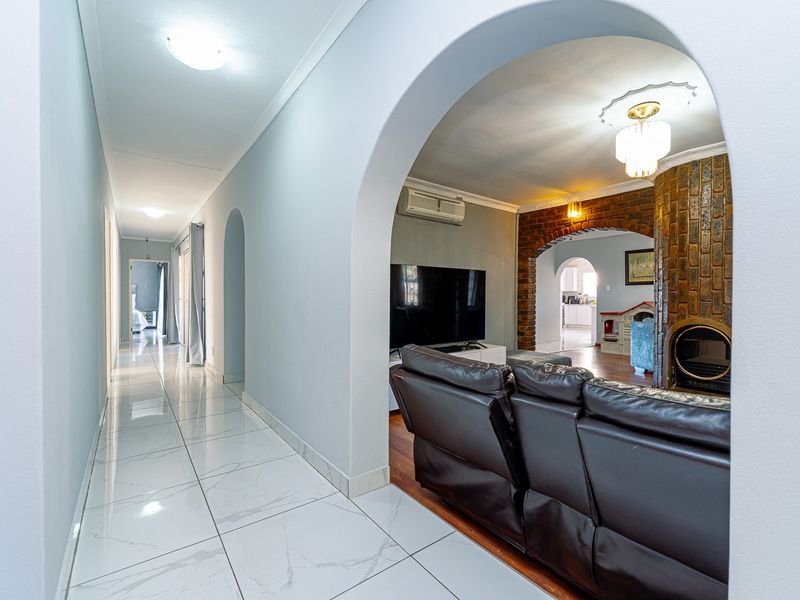 Spacious living area featuring a distinctive brick fireplace, elegant archways, and a blend of modern tiled and warm hardwood flooring.