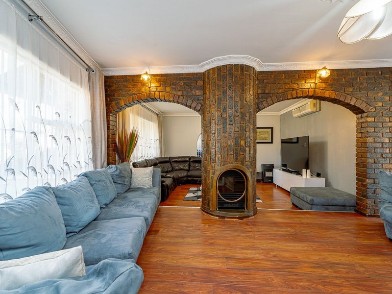 Spacious living room featuring a central brick fireplace with dual archways, laminate flooring, and decorative crown molding.
