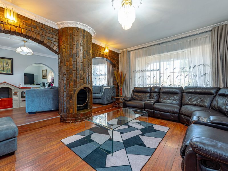 Spacious living room featuring a distinctive central brick fireplace, arched architectural details, laminate flooring, and crown molding throughout.