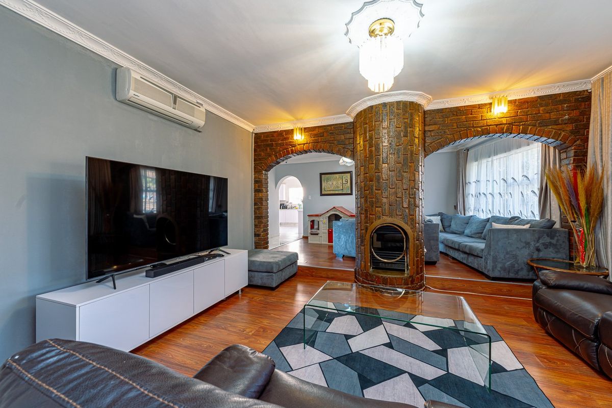 Spacious living room featuring a central brick fireplace, decorative archways, split-system air conditioning, and warm laminate flooring.