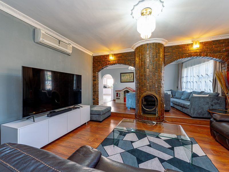 Spacious living room featuring a central brick fireplace, decorative archways, split-system air conditioning, and warm laminate flooring.