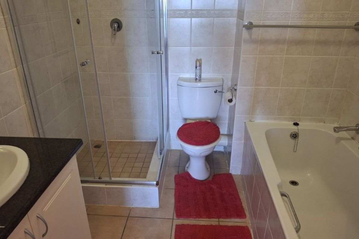 A functional bathroom featuring a separate shower enclosure, bathtub, vanity cabinet, and neutral wall tiling.