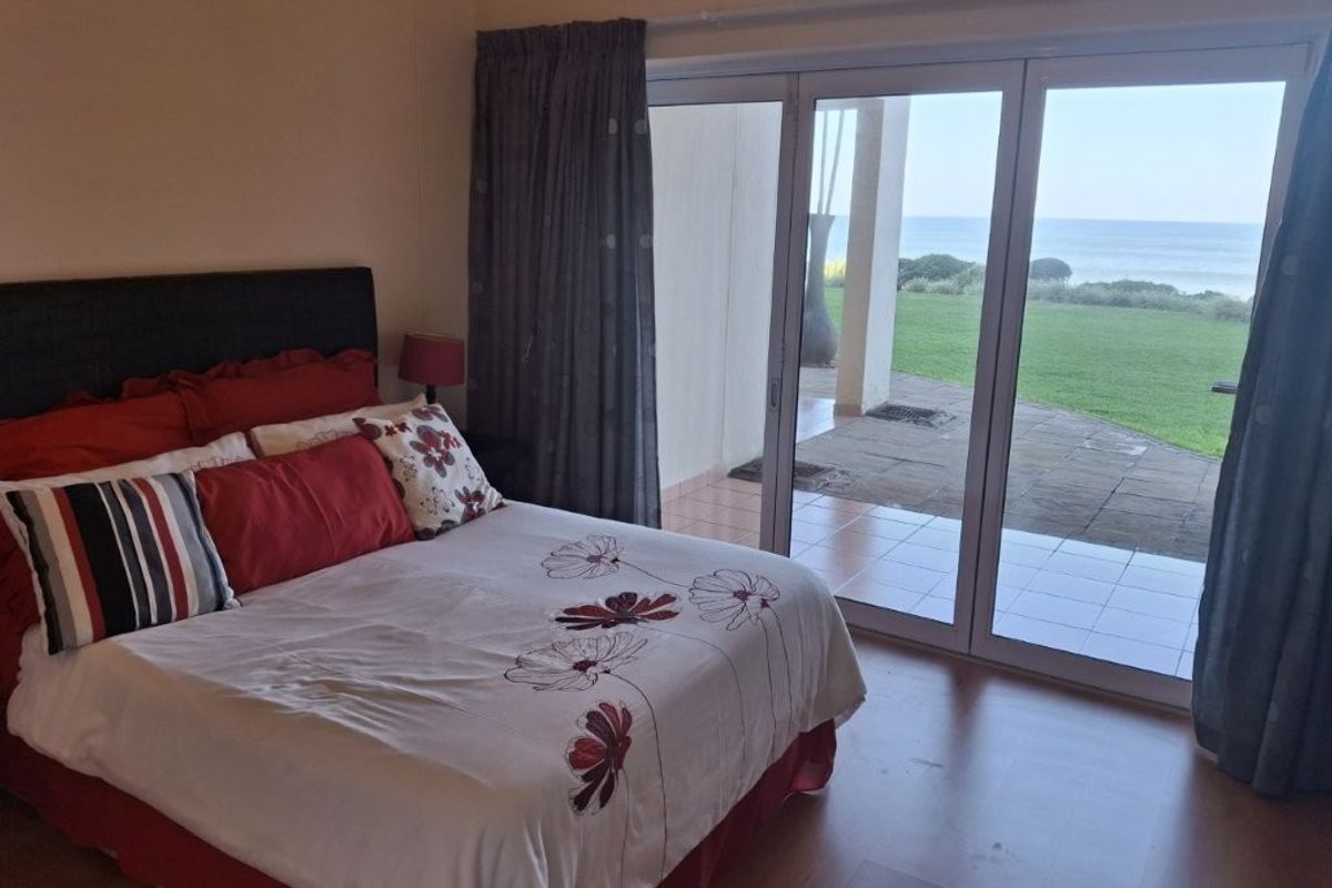 A bedroom featuring laminate flooring and large sliding glass doors that provide direct access to a patio with ocean views.