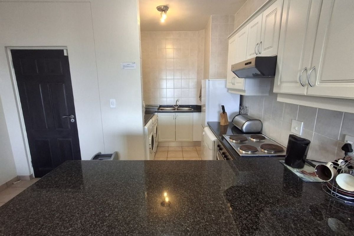 Functional kitchen featuring granite countertops, built-in cabinetry, an electric hob with extractor fan, and a double sink with tiled backsplash.