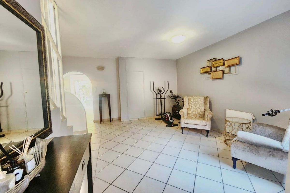 A spacious living area featuring neutral tiled flooring, an elegant archway leading to adjacent rooms, and a staircase.