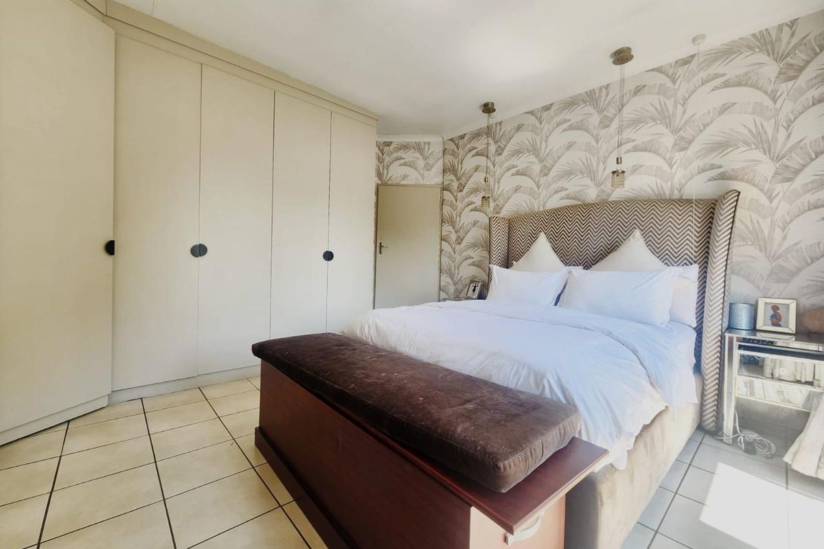 A well-maintained bedroom featuring built-in cupboards, tiled flooring, and decorative wallpaper, offering a clean and functional living space.