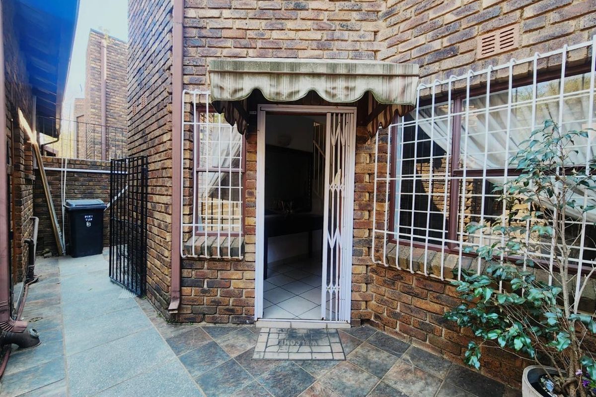 Rear exterior view of the property featuring a brick facade, tiled patio area, and security gate entrance with a protective awning.