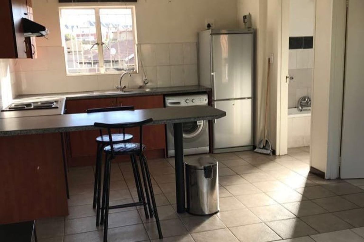 Functional kitchen featuring laminate cabinetry, breakfast bar, tiled flooring, and backsplash, offering a practical layout with direct access to adjacent rooms.