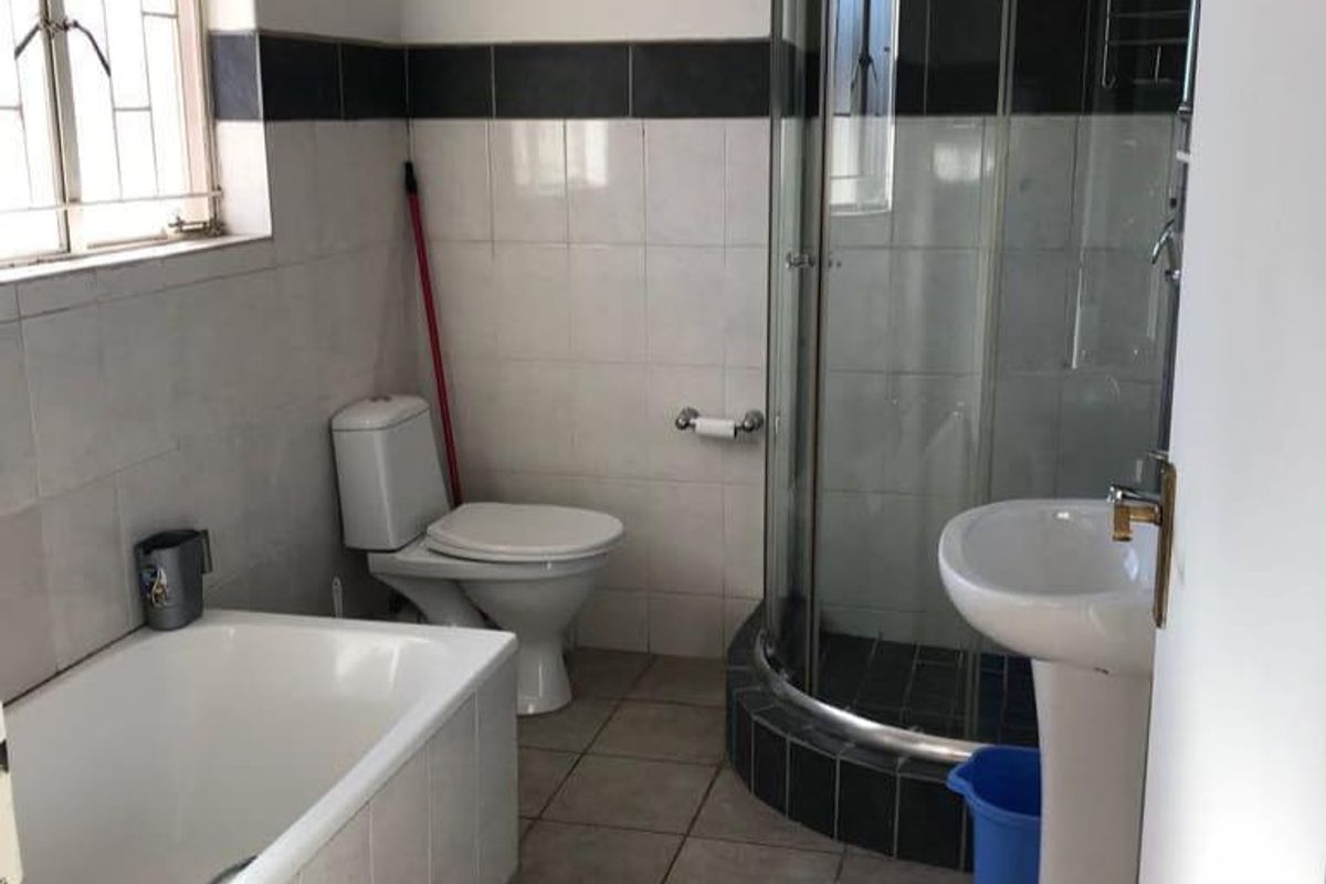 A functional bathroom featuring a built-in bathtub, a corner shower enclosure, a pedestal basin, and a toilet with neutral wall and floor tiling.
