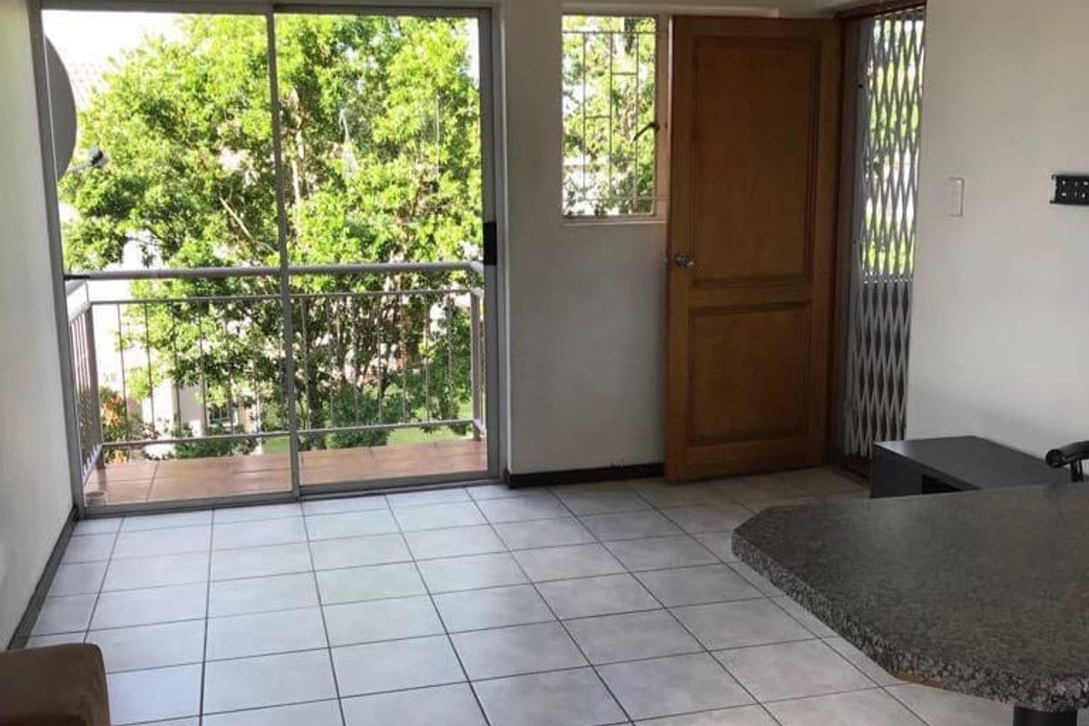 Open plan living area featuring tiled flooring, a breakfast bar, and direct access to a private balcony through sliding glass doors.