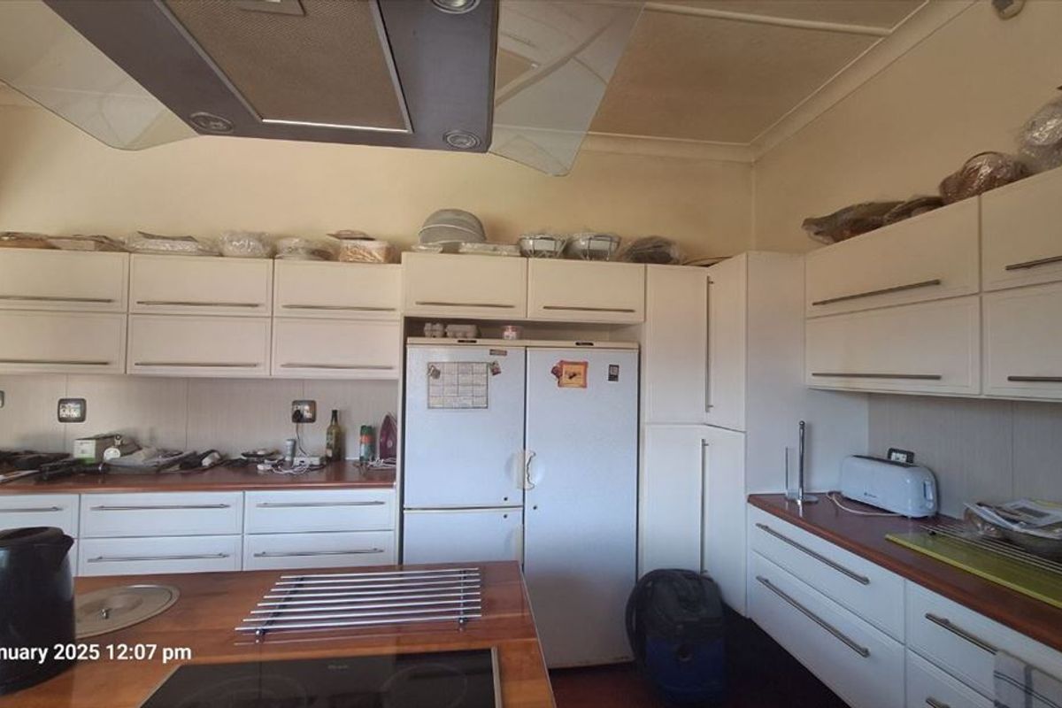 A functional kitchen featuring white built-in cabinetry, a central hob, and an overhead extractor fan with wood-look countertops.
