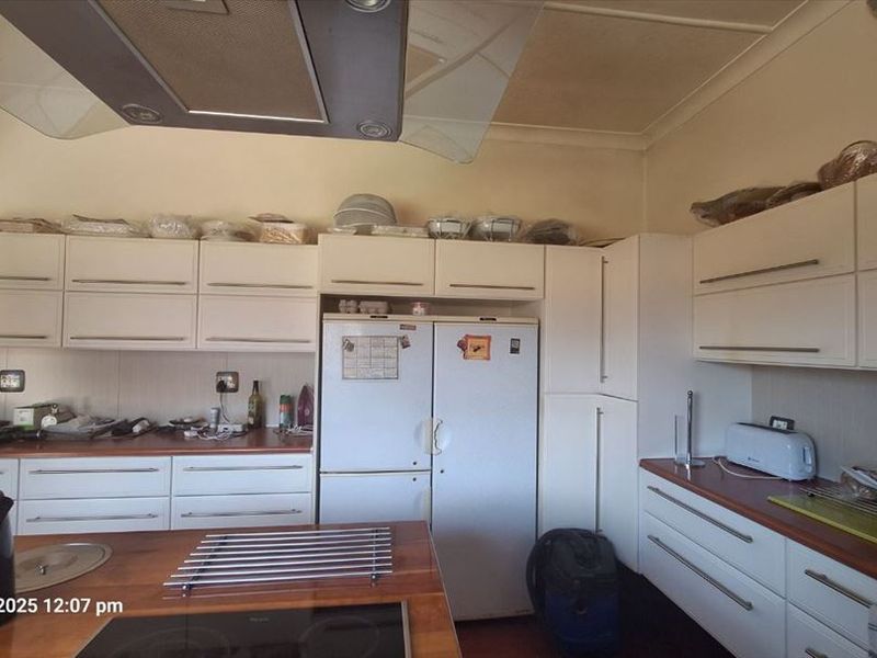 A functional kitchen featuring white built-in cabinetry, a central hob, and an overhead extractor fan with wood-look countertops.