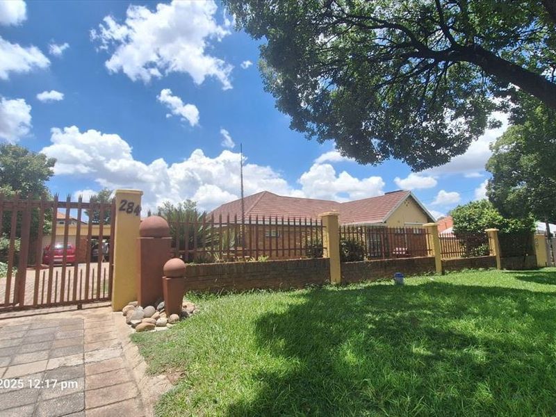 Front exterior view of the property featuring a brick boundary wall, metal driveway gate, paved driveway, and a landscaped garden area.