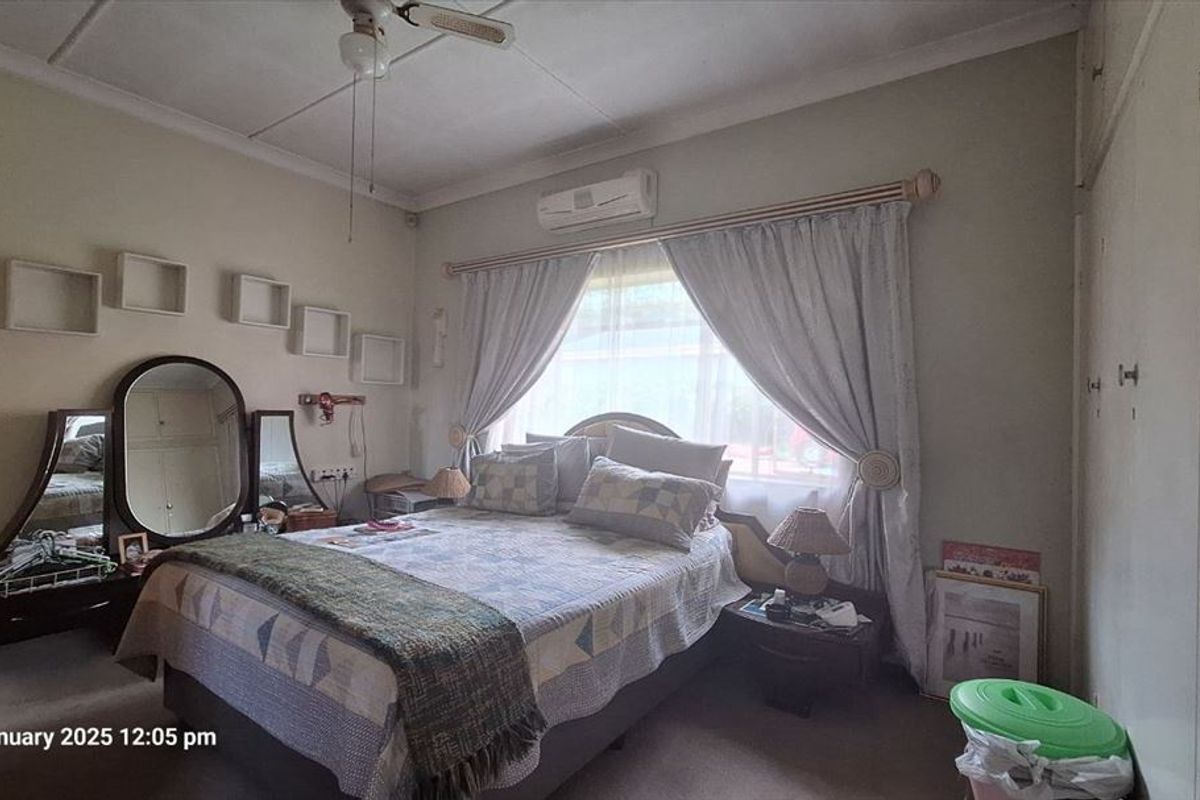 A functional bedroom featuring built-in cupboards, a ceiling fan, and a wall-mounted split-system air conditioner for climate control.