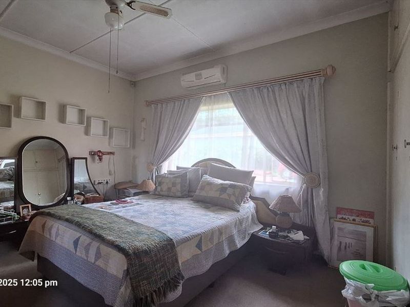 A functional bedroom featuring built-in cupboards, a ceiling fan, and a wall-mounted split-system air conditioner for climate control.