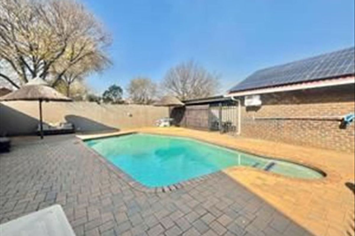 Outdoor pool area featuring a swimming pool, brick paved surround, and boundary wall, set against a brick building exterior with solar panels.