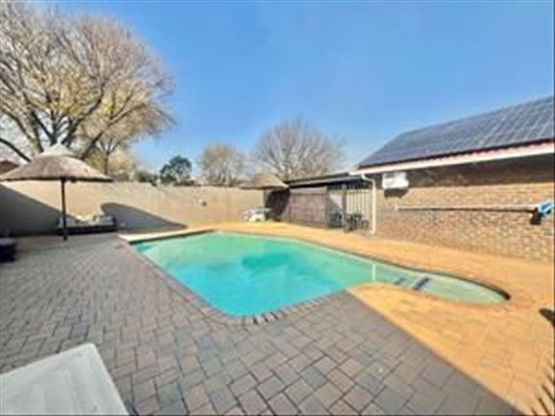 Outdoor pool area featuring a swimming pool, brick paved surround, and boundary wall, set against a brick building exterior with solar panels.